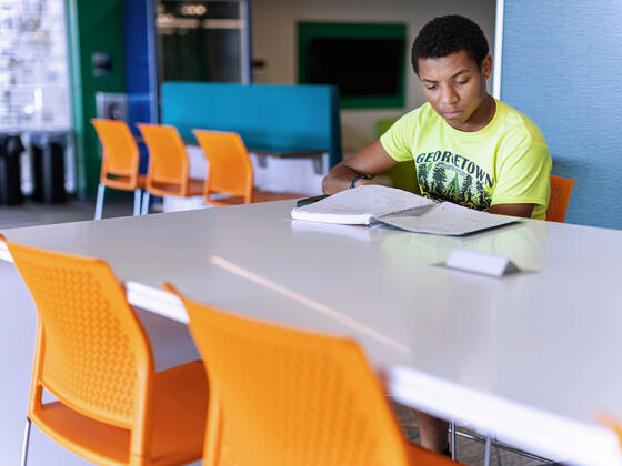 A student studying a book at a table in Roj Student Center.