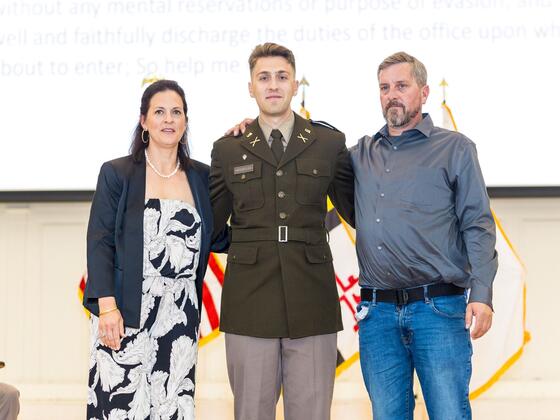 A cadet poses in between his parents on stage.