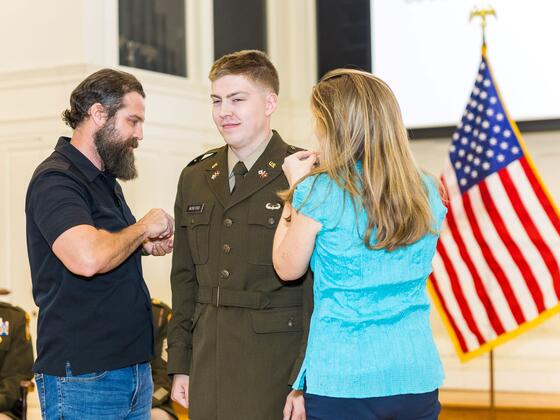 A cadet receives pins on his uniform from his mother and father.