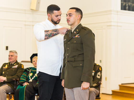 A cadet receives pins on his uniform from his brother on stage.