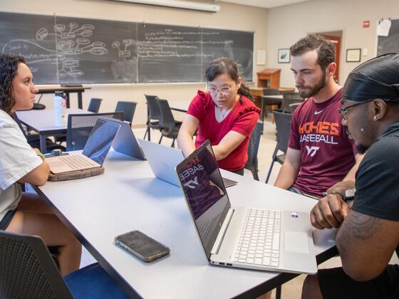 Three students sit with a professor and look at laptop screens.