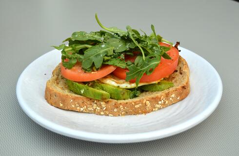 Photo of toast on a plate with an egg, tomato, and arugula on top. 