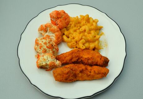 Photo of a white plate with chicken tenders, macaroni and cheese, and cauliflower on it.