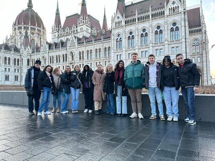 A group of students stands in front of the Hungarian Parliament Building