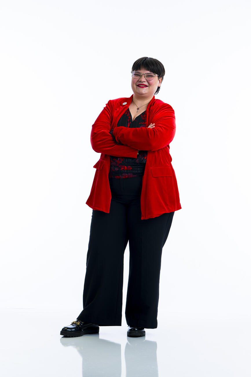 A student in a red suit stands with arms crossed in front of a white background.