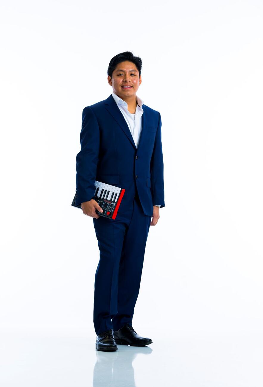 A student in a suit holds a small keyboard by their side against and white background.