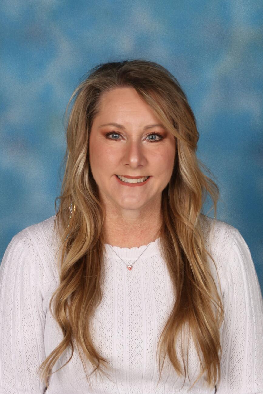 Kristina Stacey, a woman with long, blonde hair, wears a white sweater and smiles in front of a blue backdrop.