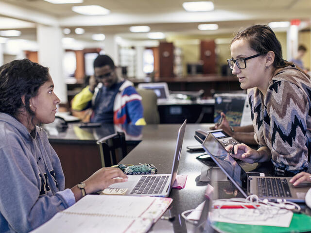 Two students with laptops speaking in Hoover Library.