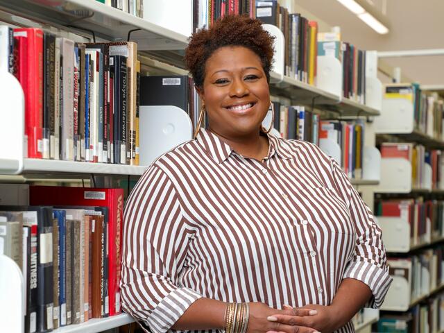 Photo of professor Shaeeda Mensah in front of a bookcase in the library.