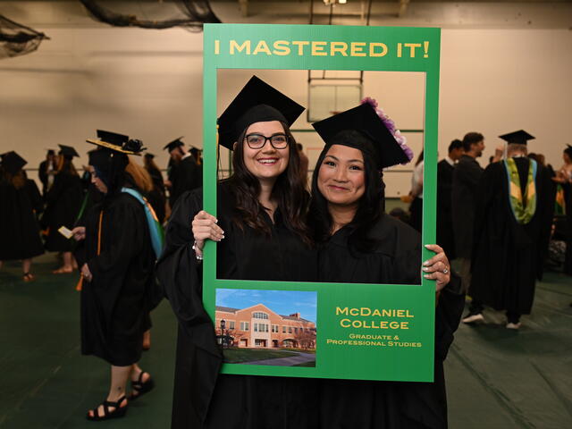 students pose in regalia with a sign that says, "I Mastered It" featuring a photo of McDaniel College