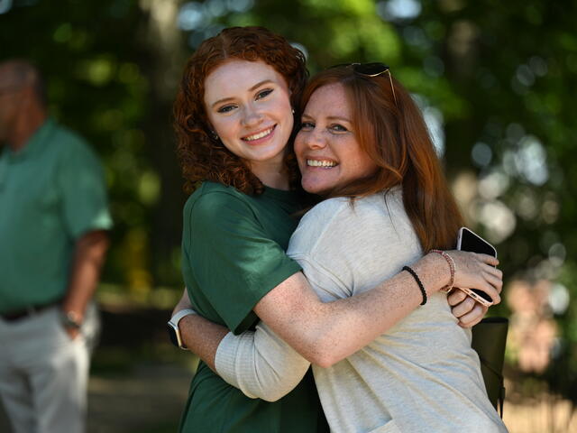 A McDaniel student hugs her mother while they both look toward the camera and smile.