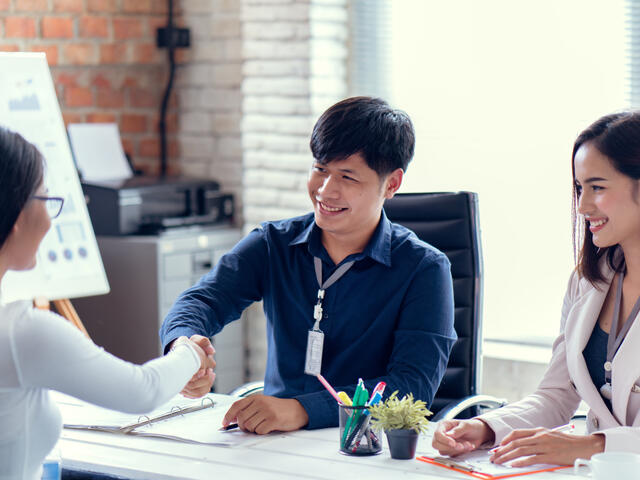 Three young adults shaking hands with a desk between them