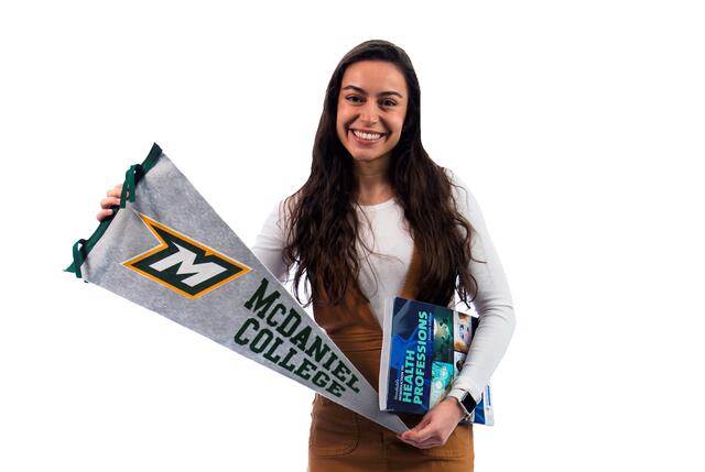 Giulia Pires poses with a McDaniel pennant and a textbook on health professions.