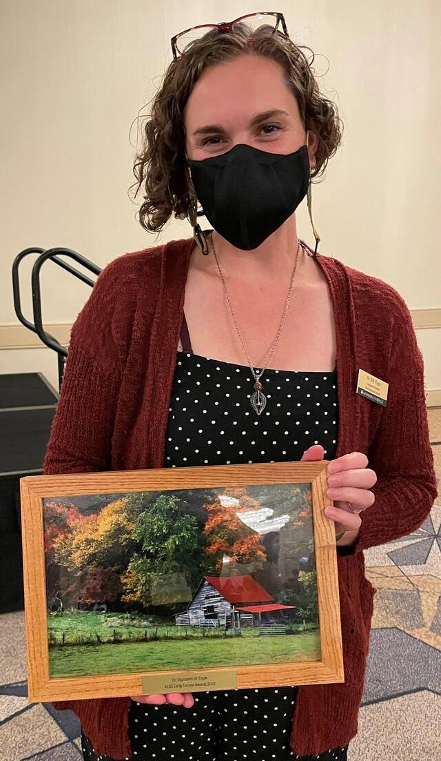 Professor Elly Engle holding her 2022 AESS Early Career Award.