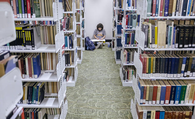 A student sits on the floor in Hoover Library between the aisle of book shelves.