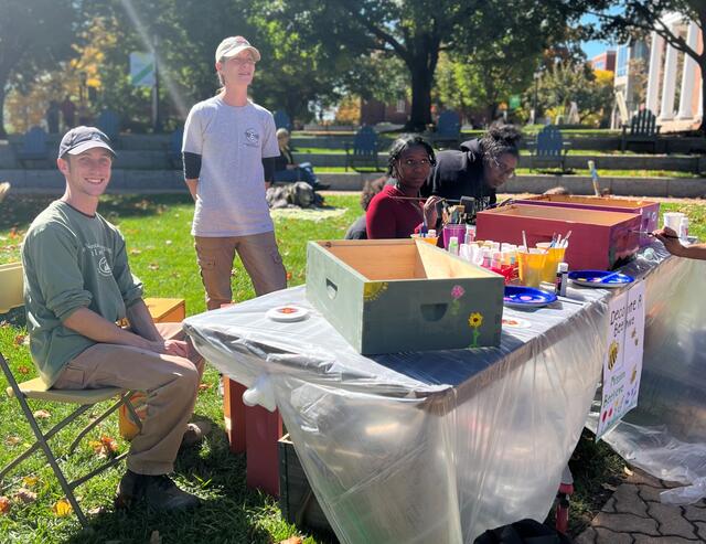 Two representatives from Mission Beelieve stand behind a table where students are painting apiary boxes.