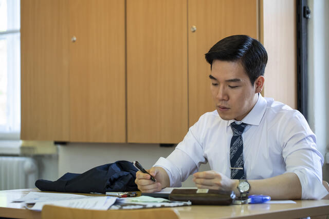 A student in a white button-down short looks at papers on a desk.