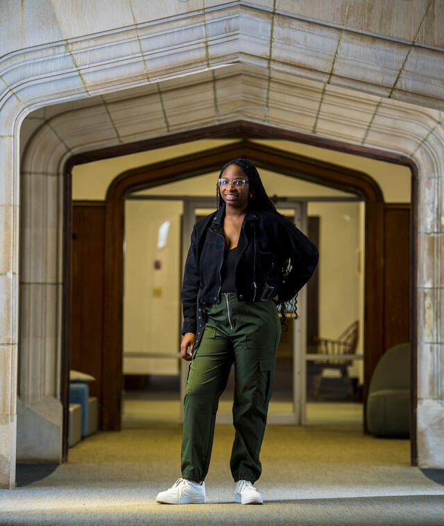 A student stands under a stone arch indoors with one hand on her hip.