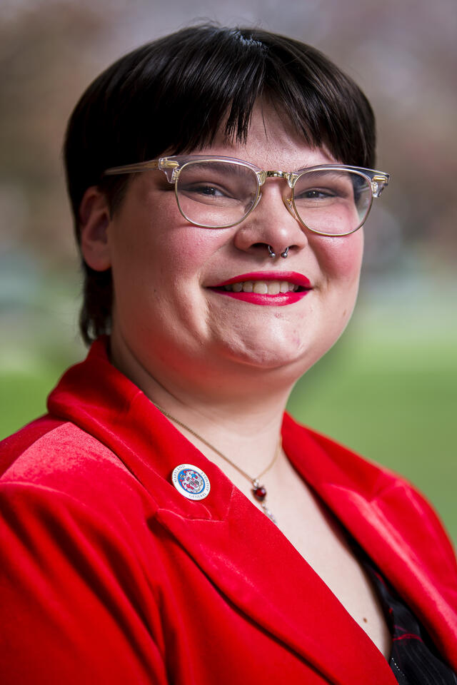 A close up headshot of a student in a red suit with a Maryland Student Legislature pin on the lapel.