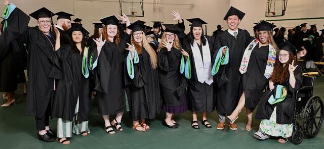 A group photo of graduates of the Deaf Education program wearing their caps and gowns and laughing.