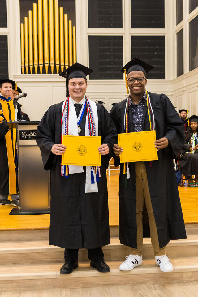 two students wearing regalia pose with awards