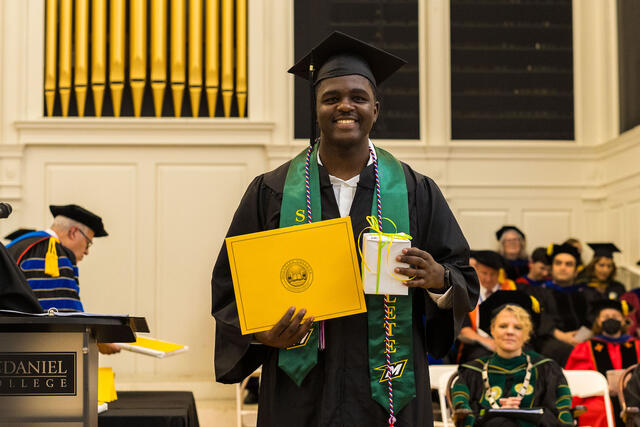 Student in graduation regalia holds up award