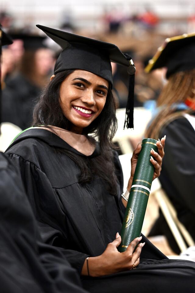 Student in graduation regalia holds up diploma tube