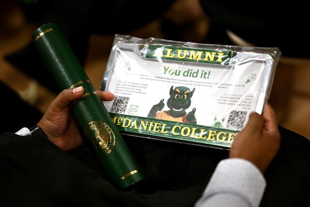 Person holds diploma tube and license plate holder that says "Alumni, McDaniel College"
