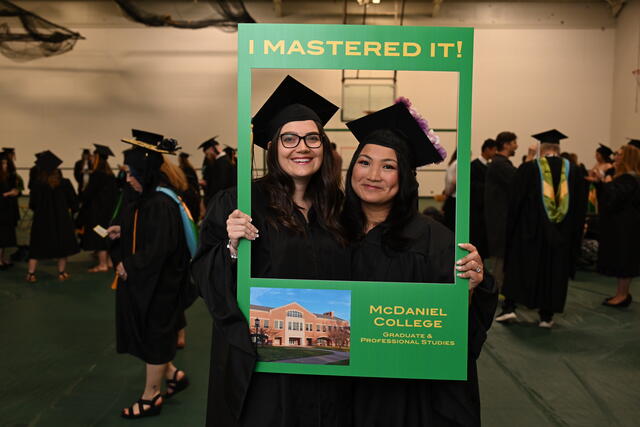 students pose in regalia with a sign that says, "I Mastered It" featuring a photo of McDaniel College