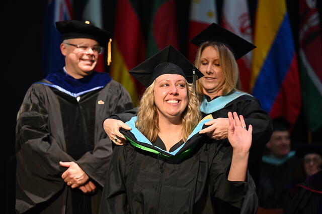 Faculty member places graduate commencement hood on student