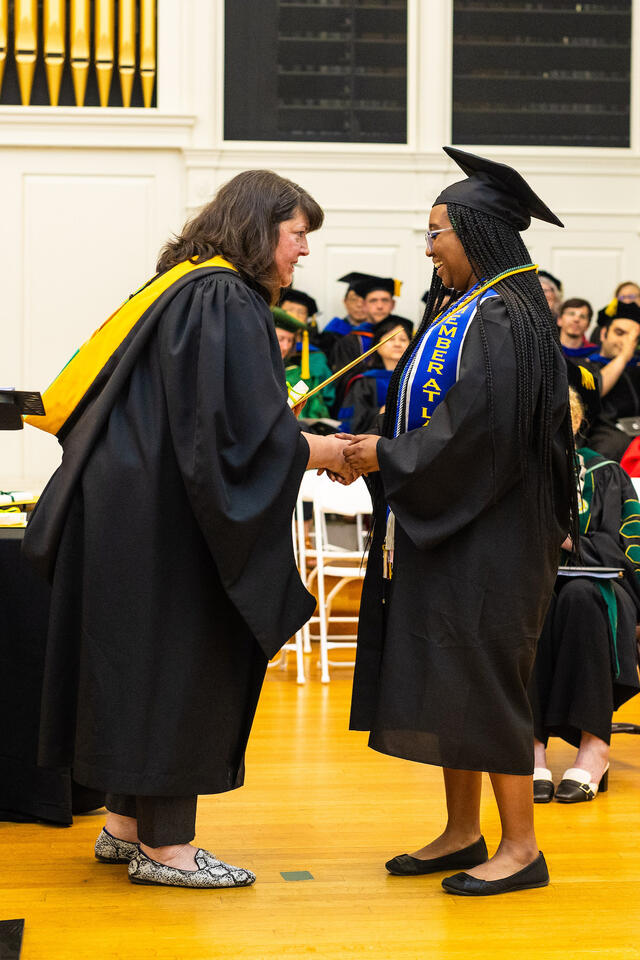 faculty member in regalia shakes hands with student in regalia