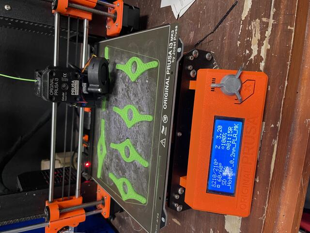 Photo of green plastic one-handed book openers on a 3D printer platform.