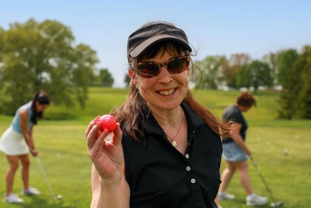 A woman holds up a pink McDaniel golf ball while standing on a golf course.