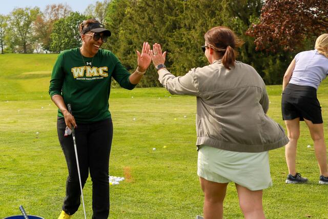 Two women high five on a golf course.