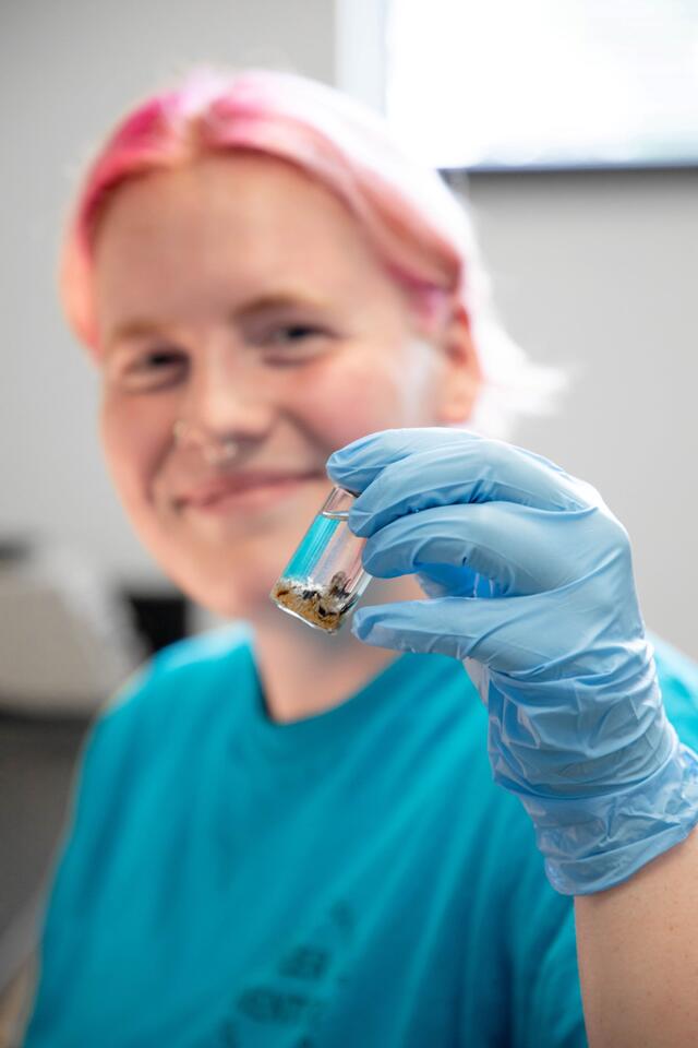 A student holds a small test tube with insects inside up to the camera.