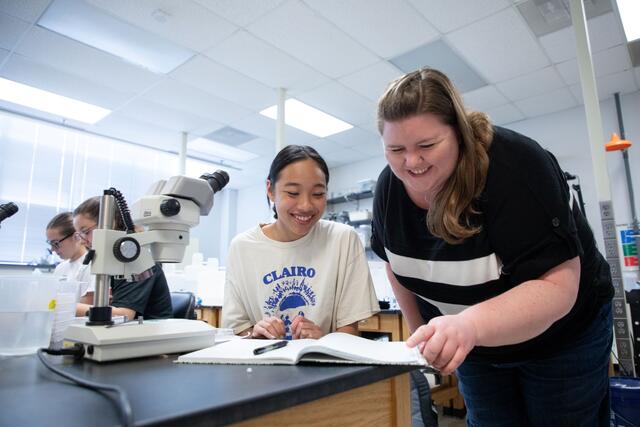 A McDaniel research student and professor look at a notebook next to a microscope.