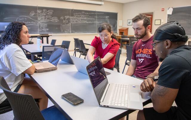 Three students sit with a professor and look at laptop screens.