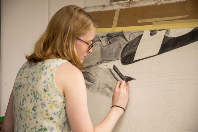 A student draws with charcoal on a canvas.