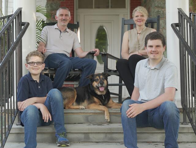 Kira the dog lies in the center of the four-person Jasken family arranged on the front steps of a house.