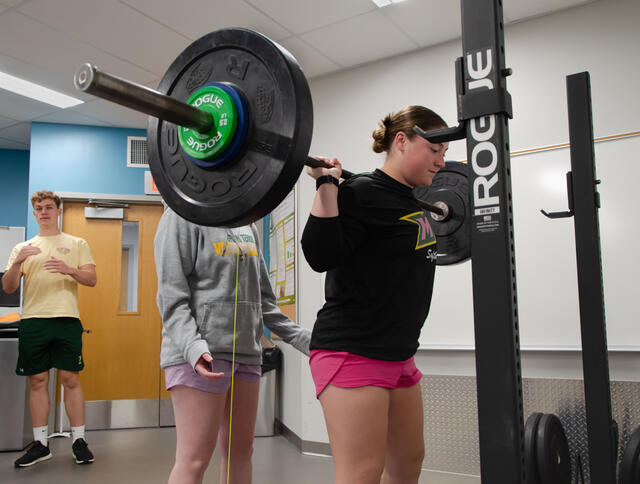 A McDaniel student uses a squat machine while two students supervise.