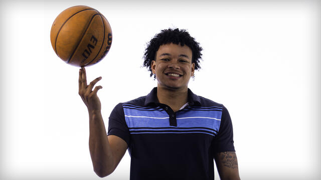 Josh Sproul spins a basketball on one hand while smiling.