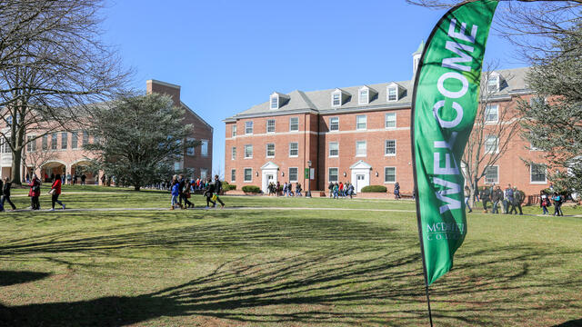 Welcome Flag with campus building and people in background