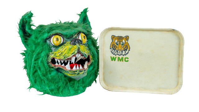 The head of the 90s Green Terror mascot head is displayed next to a WMC dining tray.