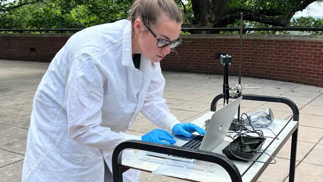 Student Angalyn Strouse looks at her laptop outside, where it is connected to a UV sensor.