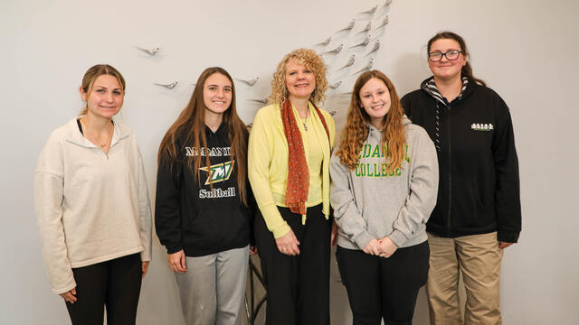 Five women stand together for a photo in front of a white wall with bird decals.