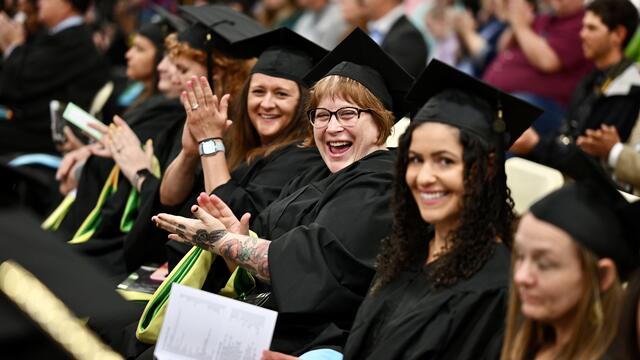 Group of students in commencement regalia sit in chairs