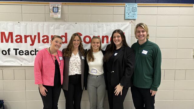 Four Education students and a faculty member pose in front of a banner that reads Maryland Council of Teachers of Mathematics.