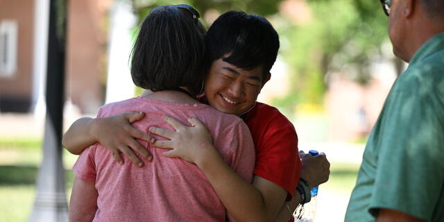 A student hugs a family member while smiling outside on the McDaniel campus.