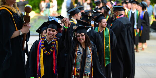 Students in graduation regalia walk in a line